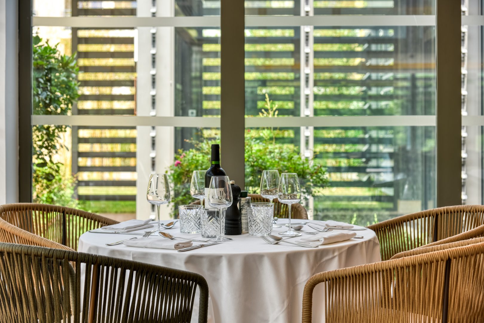 Table de restaurant placée devant une grande baie sur la terrasse végétalisée.