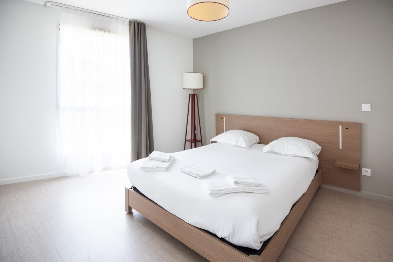 Chambre double avec lit, lampadaire et grande baie vitrée.