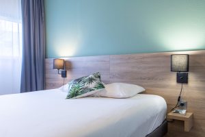 Chambre avec lit double, coussin à motif vert et mur bleu-vert.