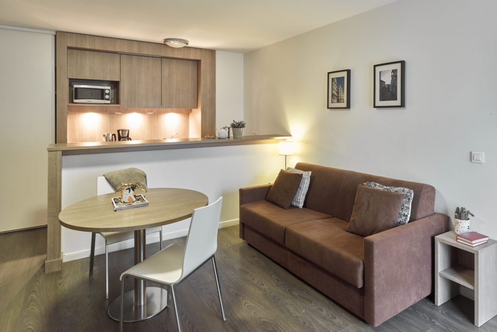 Séjour avec canapé marron, table ronde et kitchenette.