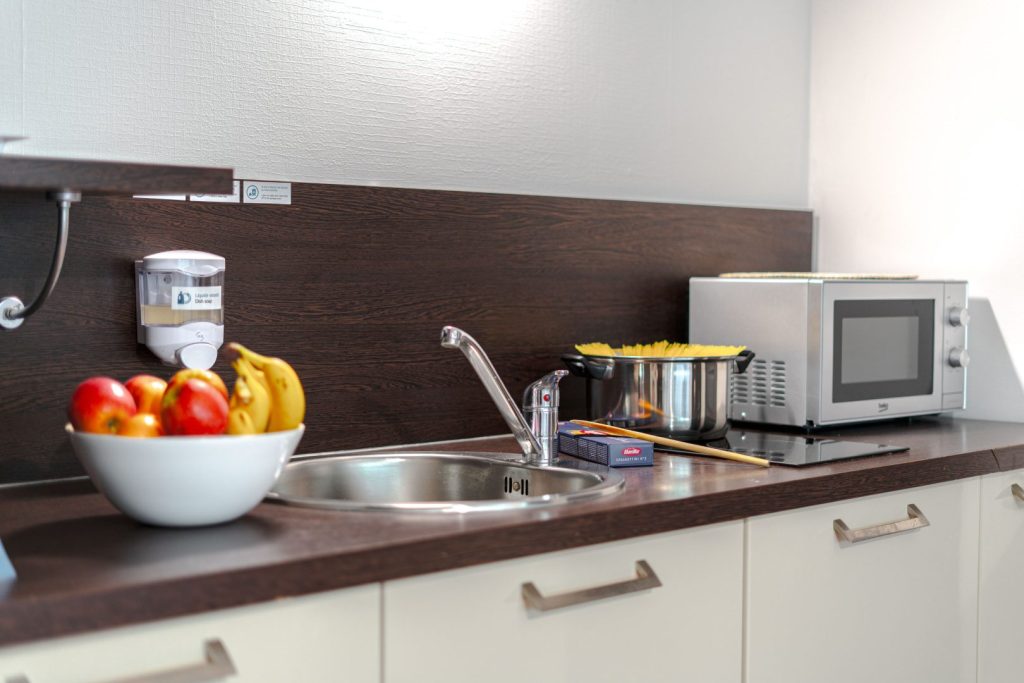 Cuisine équipée avec évier, micro-ondes et panier de fruits.