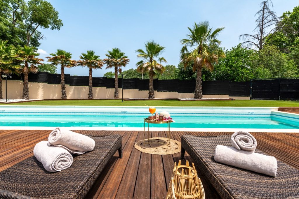 Piscine extérieure entourée de palmiers et transats avec serviettes.