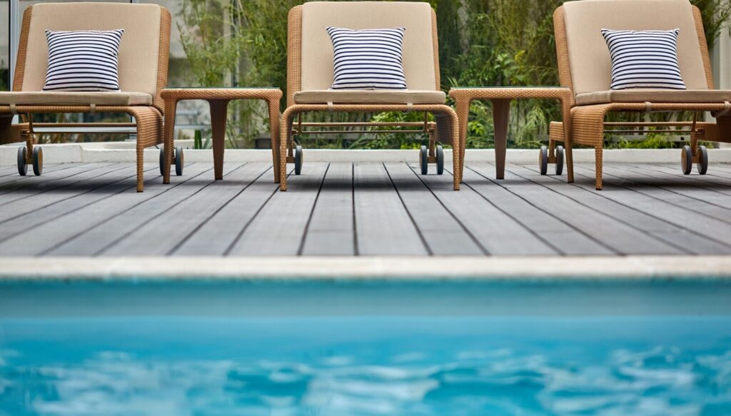 Transats en rotin avec coussins rayés blancs et noirs au bord de la piscine.