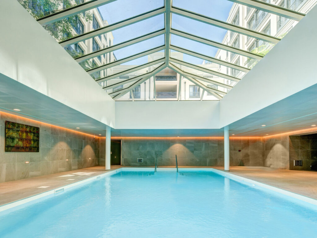 Piscine intérieure avec toit vitré et lumière naturelle, dans un cadre élégant.