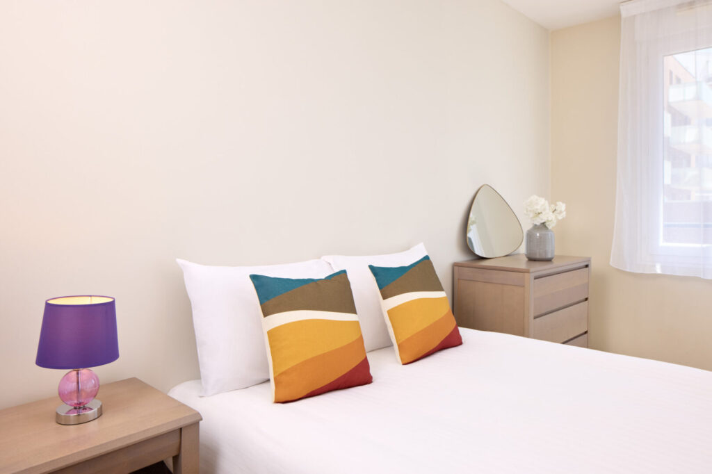 Chambre double avec coussins jaunes et terracotta, commode et miroir.