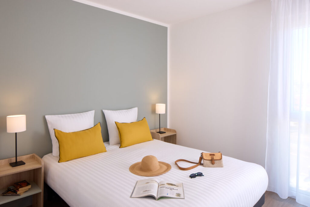 Chambre parentale avec mur vert et coussins jaunes au Zenitude Hôtel-Résidences Plérin