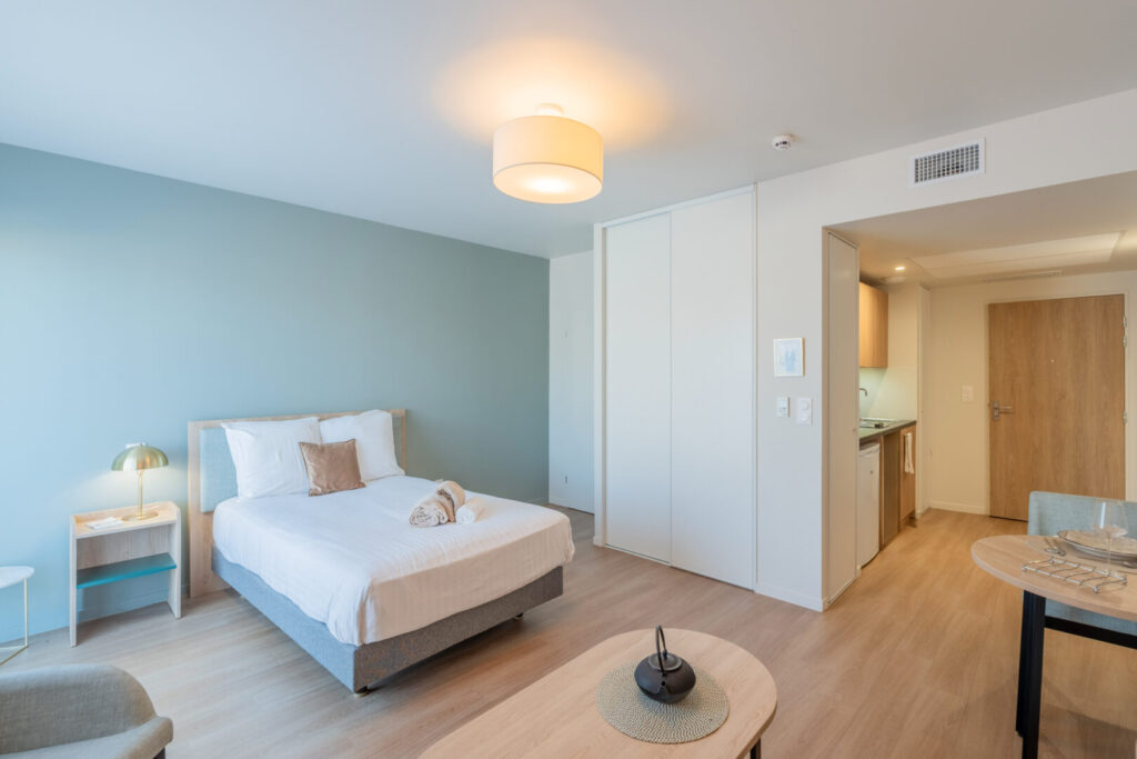 Vue intérieure d'un studio moderne : chambre, kitchenette et entrée.