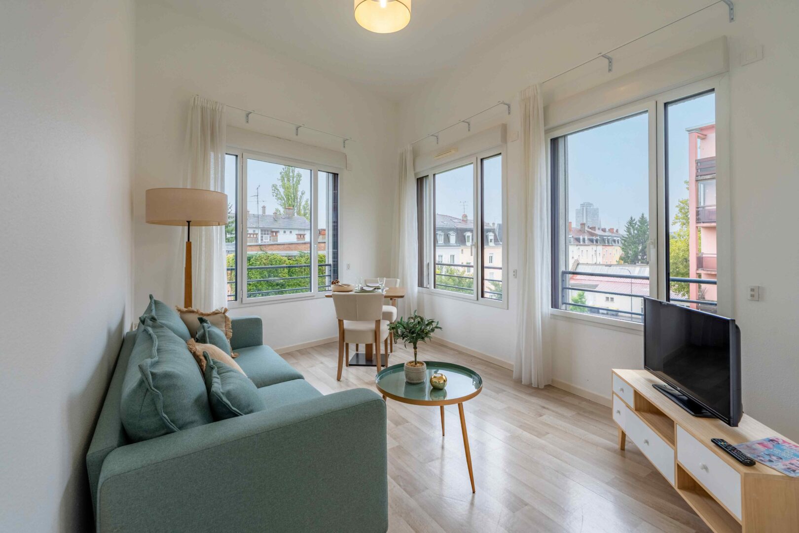 Salon lumineux avec canapé menthe, table basse ronde et vue dégagée par de grandes fenêtres.