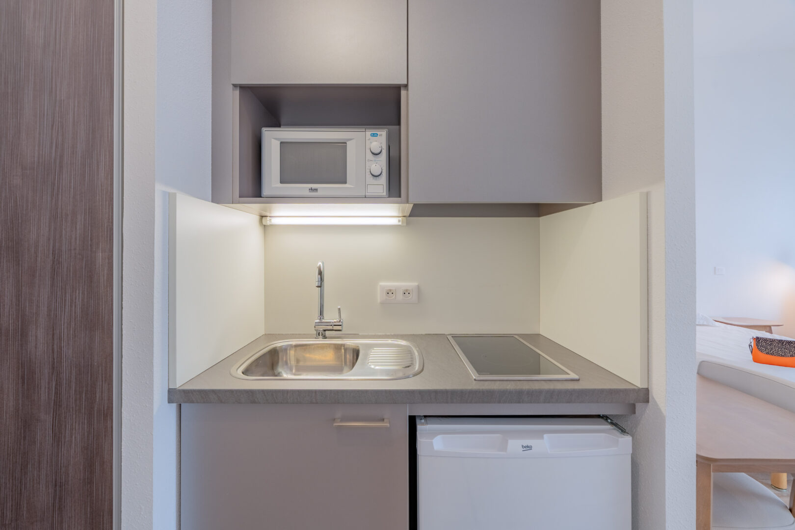 Cuisine compacte équipée avec évier, plaques de cuisson, micro-ondes et réfrigérateur.