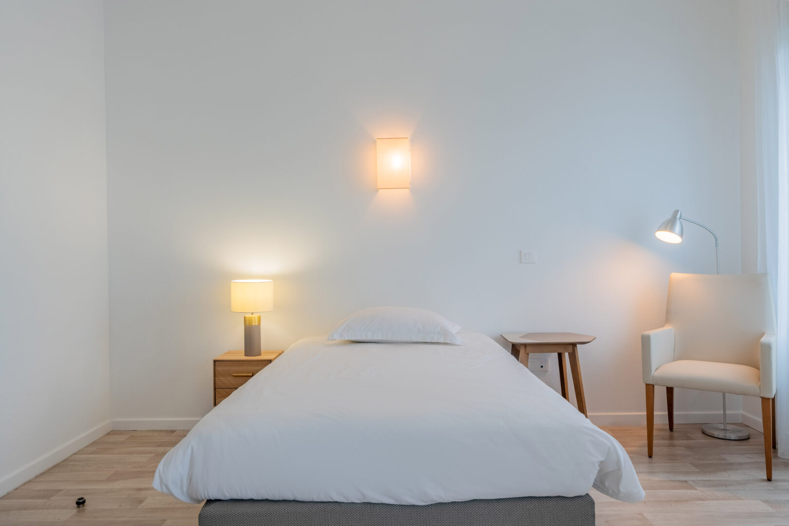 Chambre minimaliste avec lit simple, table de chevet et lampe.