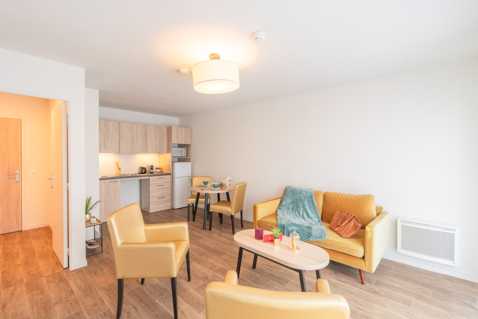 Salon avec fauteuils jaunes, table basse et coin cuisine en arrière-plan.