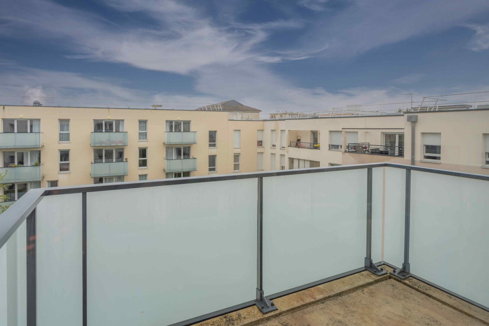 Balcon avec rambarde vitrée et vue sur les bâtiments alentours.