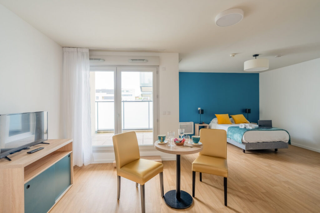 Salle à manger et lit dans une pièce lumineuse avec murs bleu et blanc.