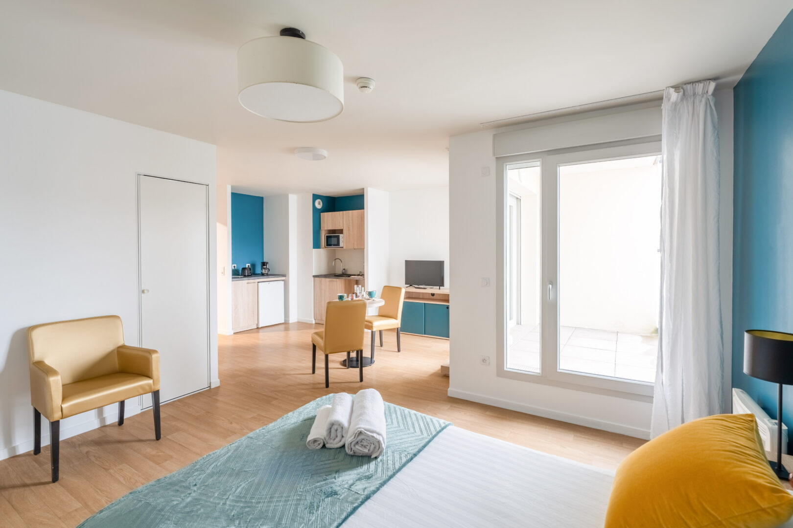 Chambre donnant sur la pièce principale lumineuse avec coin cuisine, table et espace nuit.