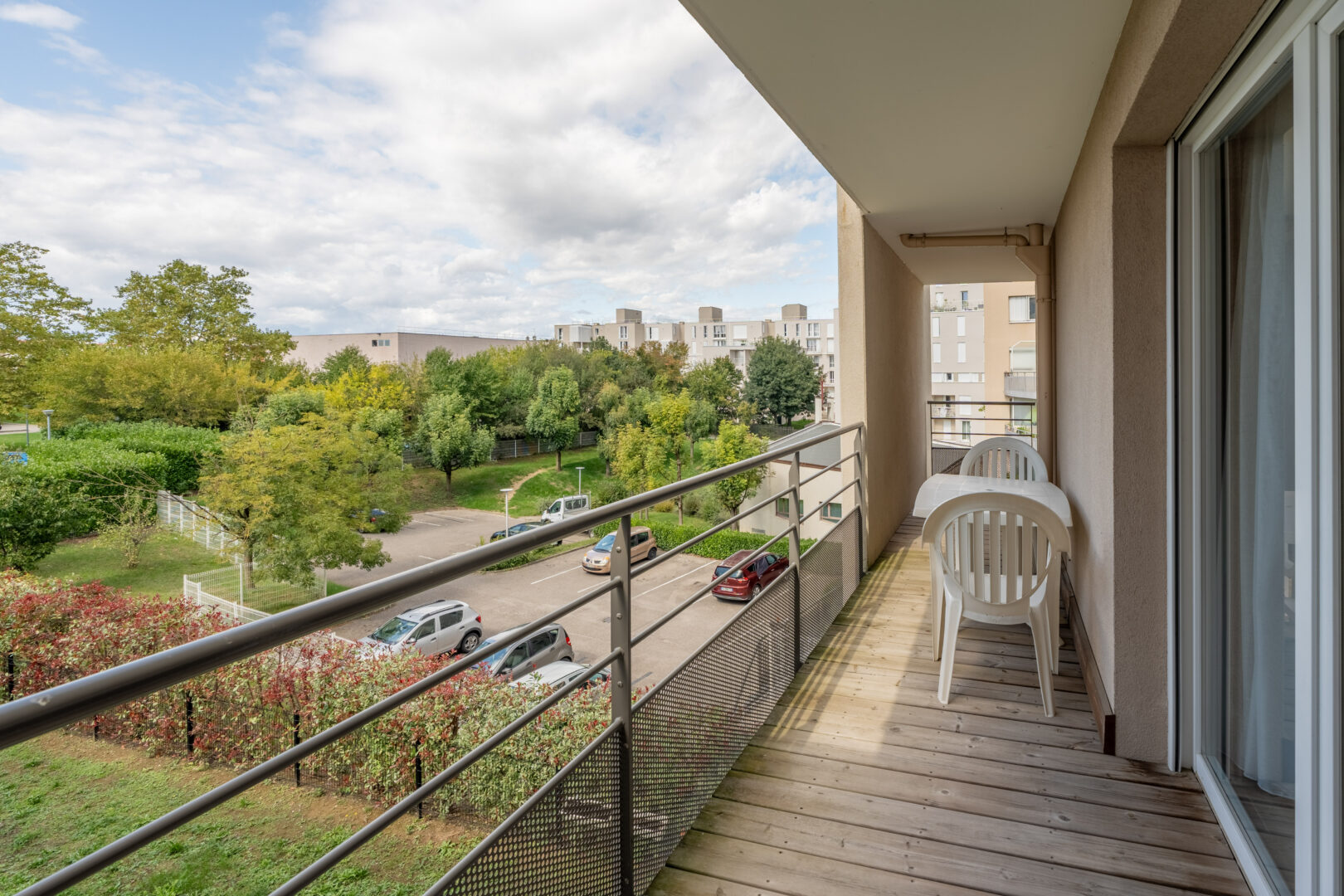 Balcon avec chaise blanche et vue dégagée sur espaces verts et la ville.