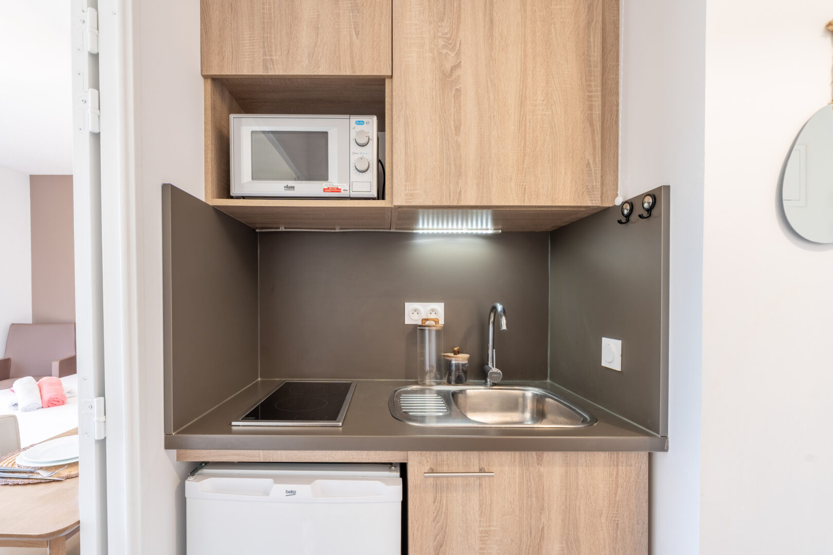 Kitchenette moderne équipée de plaques, évier, micro-ondes et rangements bois clair.