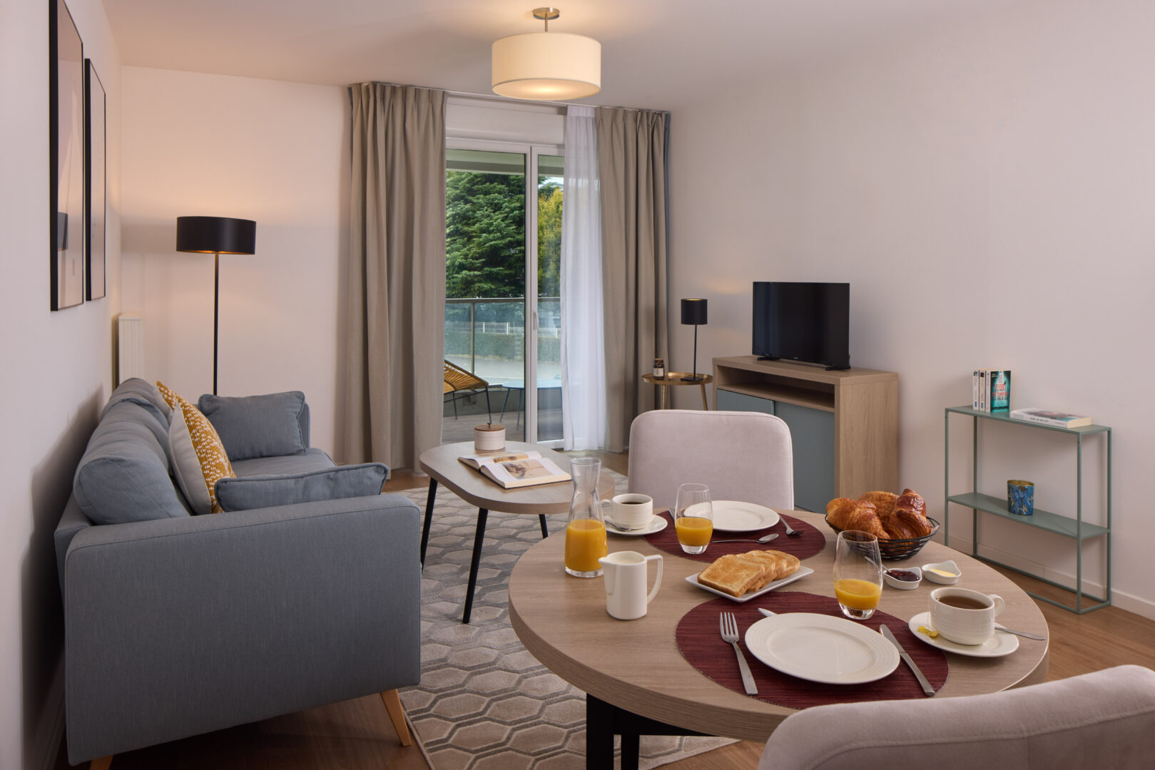 Salle à manger avec table dressée pour le petit déjeuner, fauteuils et vue sur l’extérieur.