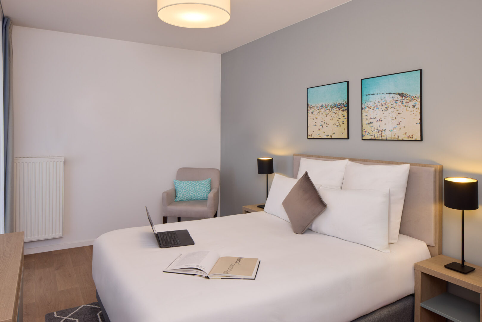 Chambre cosy avec lit double, coussins, fauteuil et tableaux décoratifs.