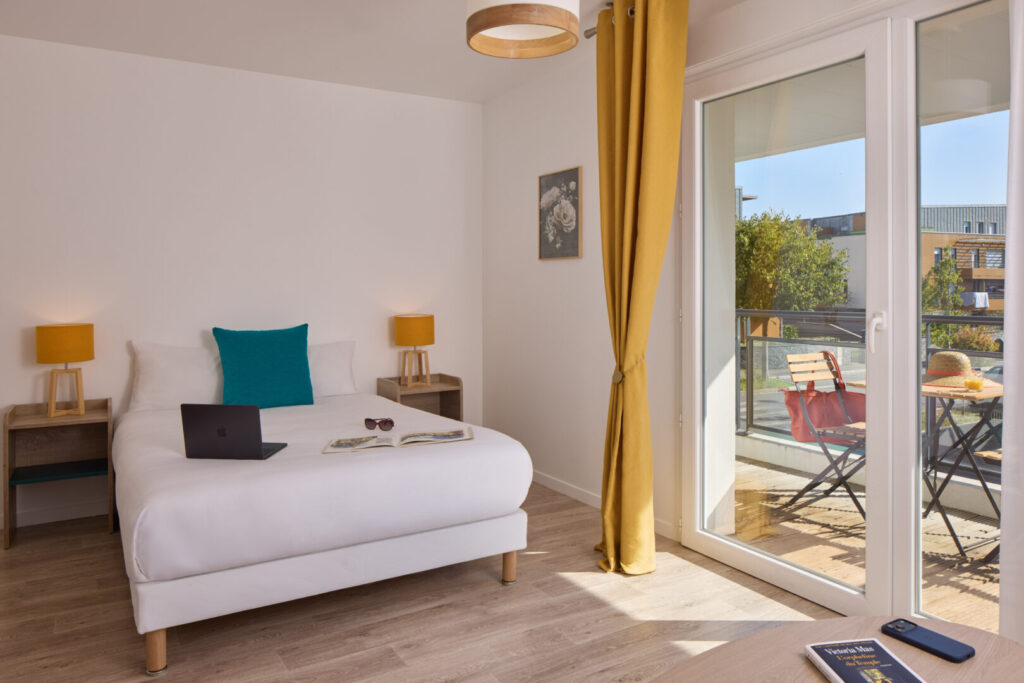 Chambre lumineuse ouvrant sur le balcon avec un lit double.