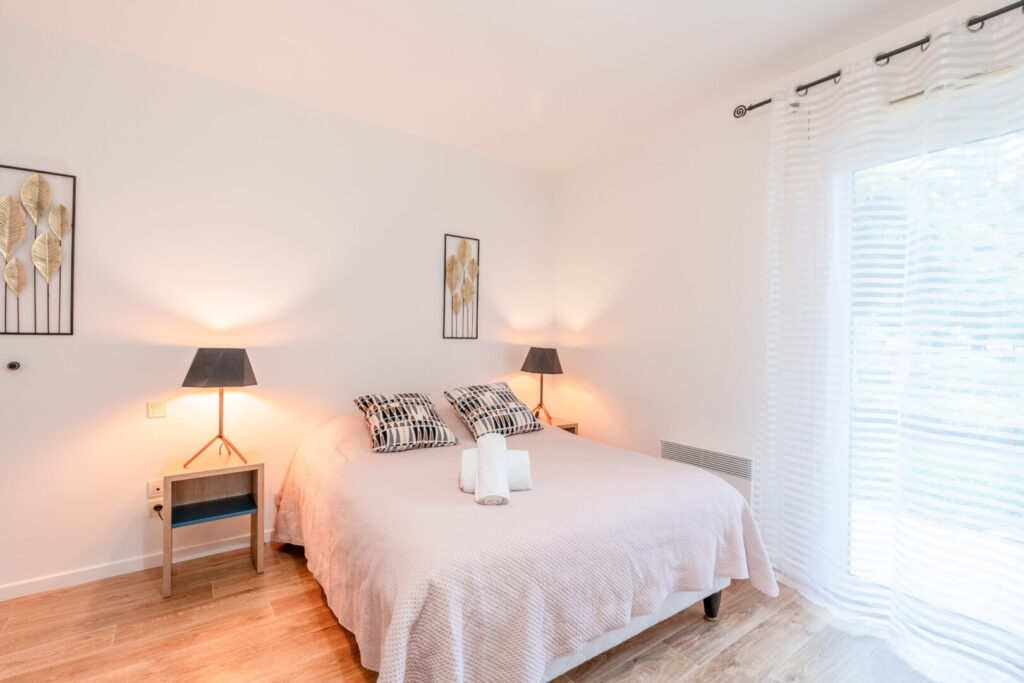 Chambre double cosy avec couette claire, coussins imprimés, lampes de chevet et décoration épurée.