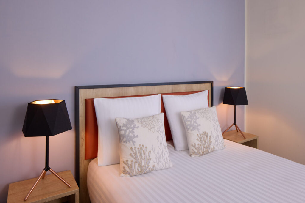 Chambre double avec mur bleu pastel, décor minimaliste, lit confortable et lampes de chevet.