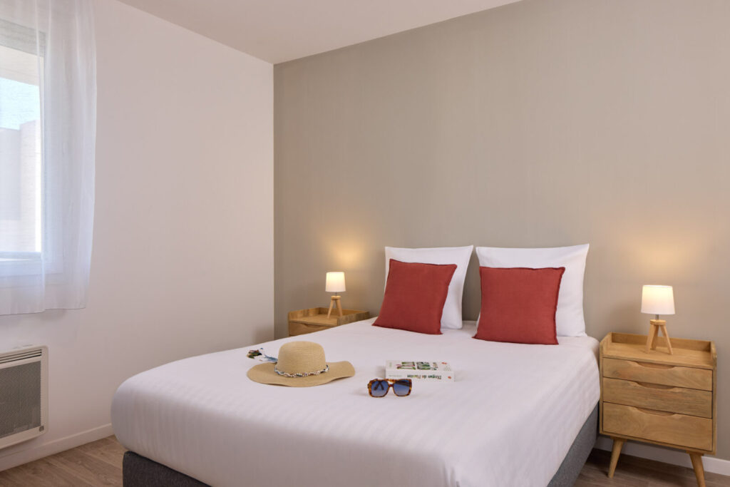 Chambre double moderne avec mur taupe, coussins rouges et lampes de chevet.