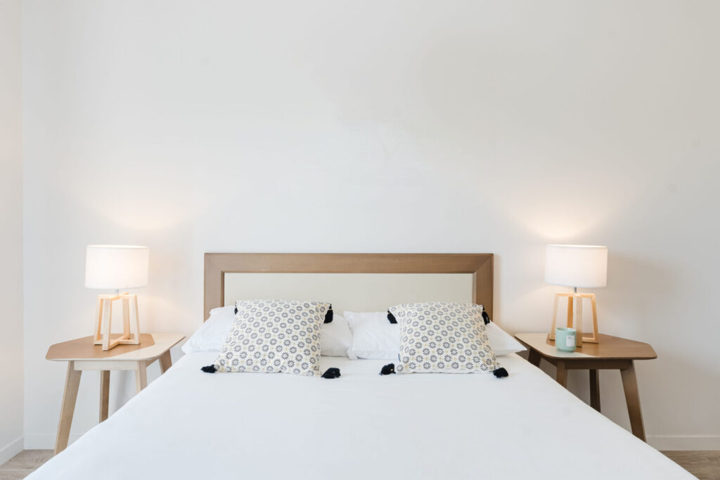 Chambre double moderne avec cadre de lit en bois, lampes de chevet et coussins clairs.