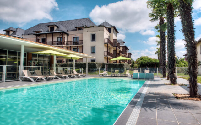 Piscine extérieure bordée de transats et de palmiers au Comfort Aparthotel Lourdes l'Acacia.