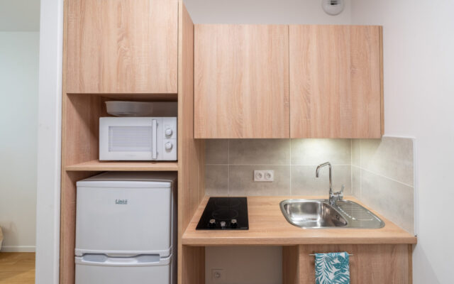 Cuisine équipée avec micro-ondes, plaques, réfrigérateur et rangements.