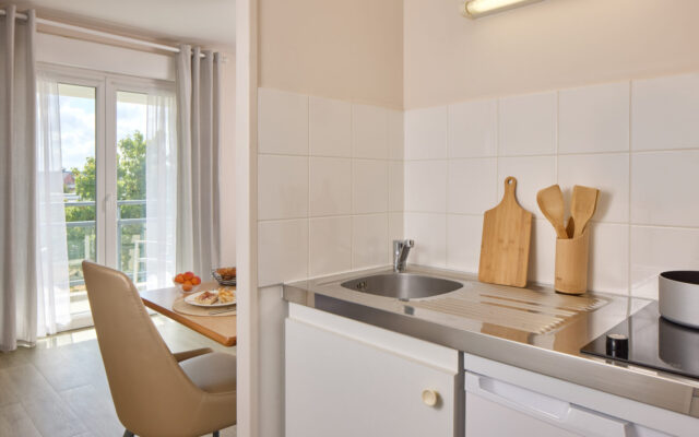 Cuisine équipée avec évier, plaques de cuisson, plan de travail et coin repas près de la fenêtre.