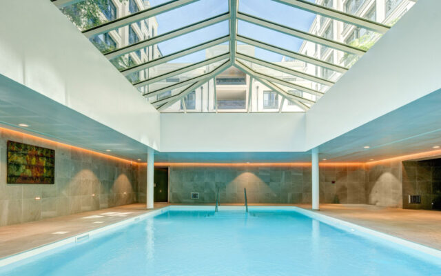 Piscine intérieure avec toit vitré et lumière naturelle, dans un cadre élégant.