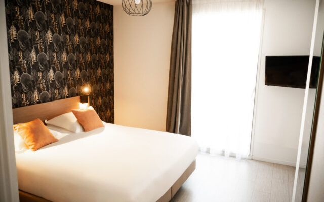 Chambre d'hôtel moderne avec lit double, coussins orange et papier peint géométrique noir.