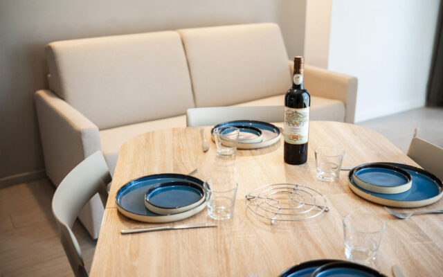Appartement moderne avec canapé beige, coin repas pour quatre et bureau TV.