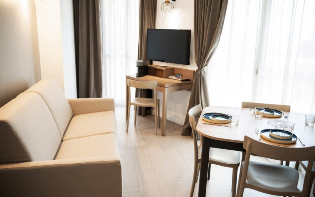 Appartement moderne avec canapé beige, coin repas pour quatre et bureau TV.
