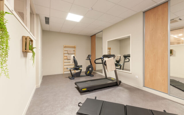 Salle de sport avec tapis de course, vélo et équipements de fitness modernes.