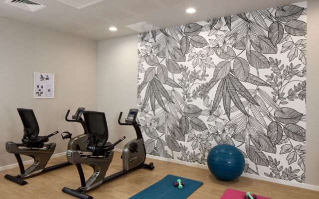 Salle de sport équipée avec vélos d’exercice, tapis de yoga et mur décoratif végétal.